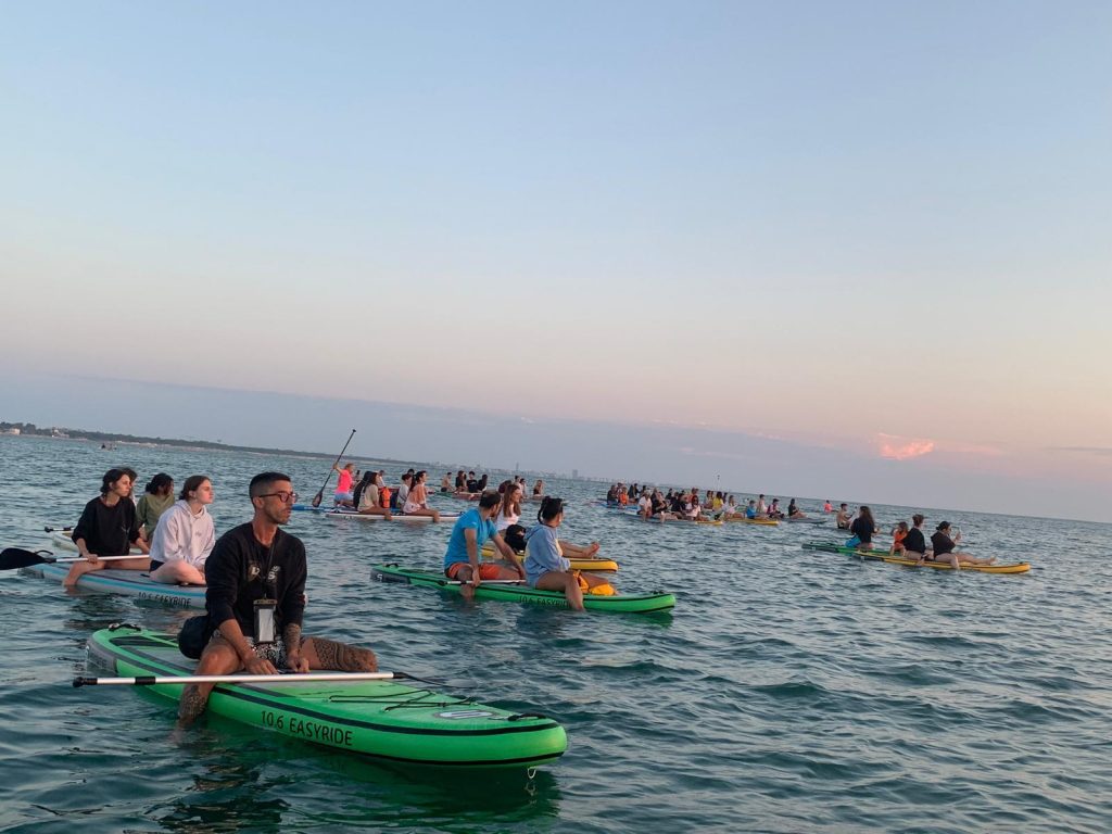 I Giovani Soci RomagnaBanca in fila sulle tavole SUP durante l'alba a Cesenatico