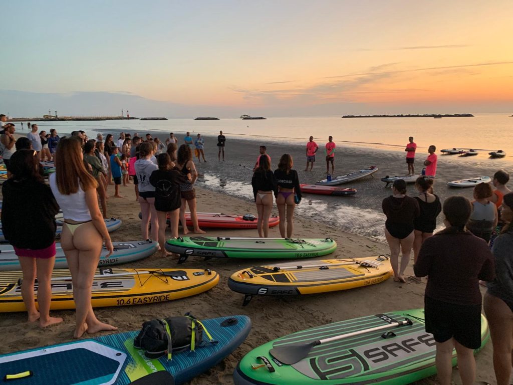 Giovani Soci RomagnaBanca radunati sulla spiaggia di Cesenatico tra le tavole SUP, con le scogliere sullo sfondo