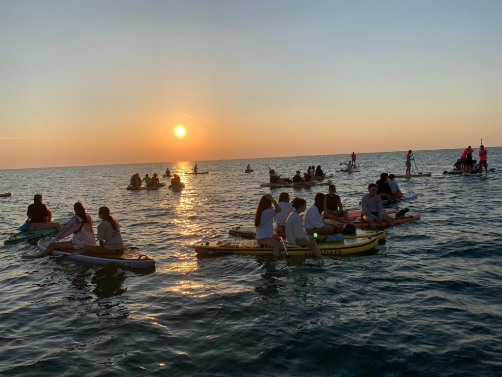 Giovani Soci RomagnaBanca seduti su tavole SUP affiancate al largo di Cesenatico durante l'alba
