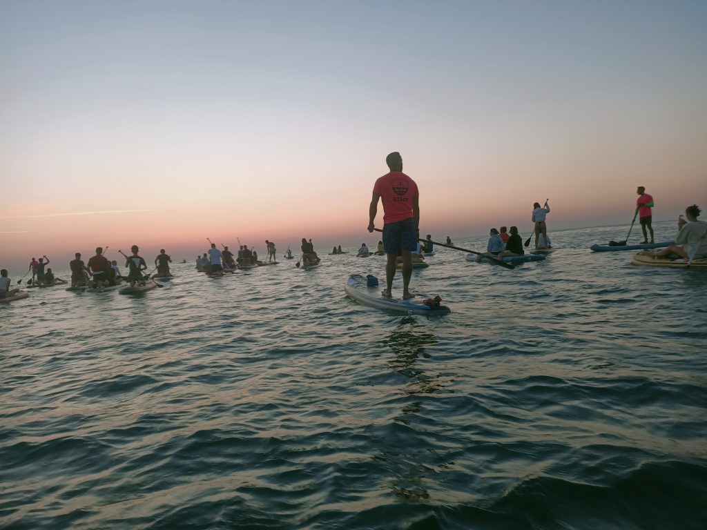 Un istruttore della Functional Sup Tribe guida il gruppo dei Giovani Soci RomagnaBanca in mare durante l'alba a Cesenatico