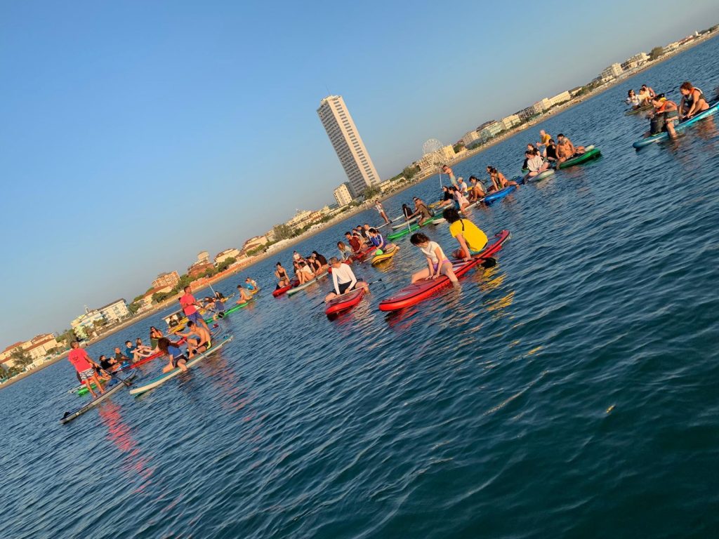 Giovani Soci RomagnaBanca rientrano in SUP verso la costa di Cesenatico dopo l'alba, con lo skyline sullo sfondo